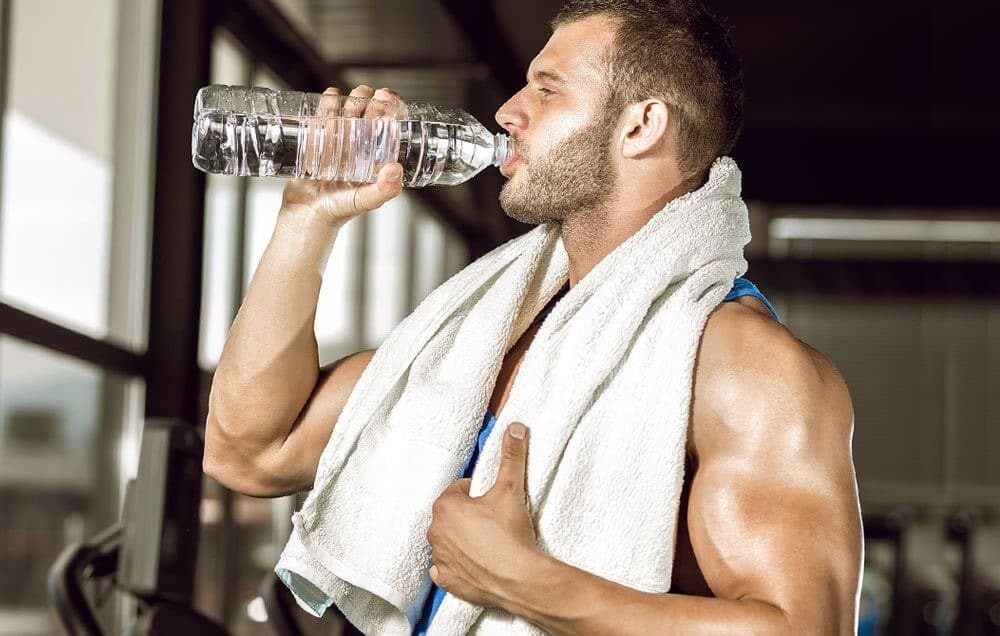 Muscular man with towel around neck, drinking a water bottle. What’s Stopping You From Getting the Gains You Want: 5 Ways You Are Negatively Impacting Your Gains