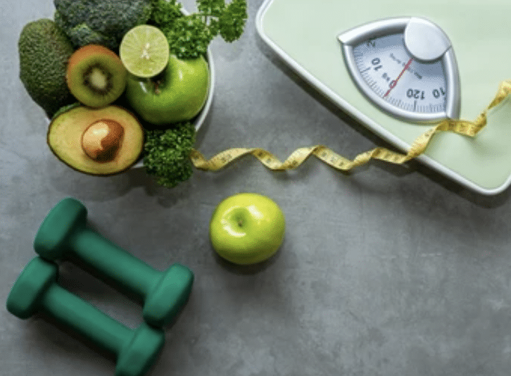 weight scale next to apple, dumbells, and fruit basket